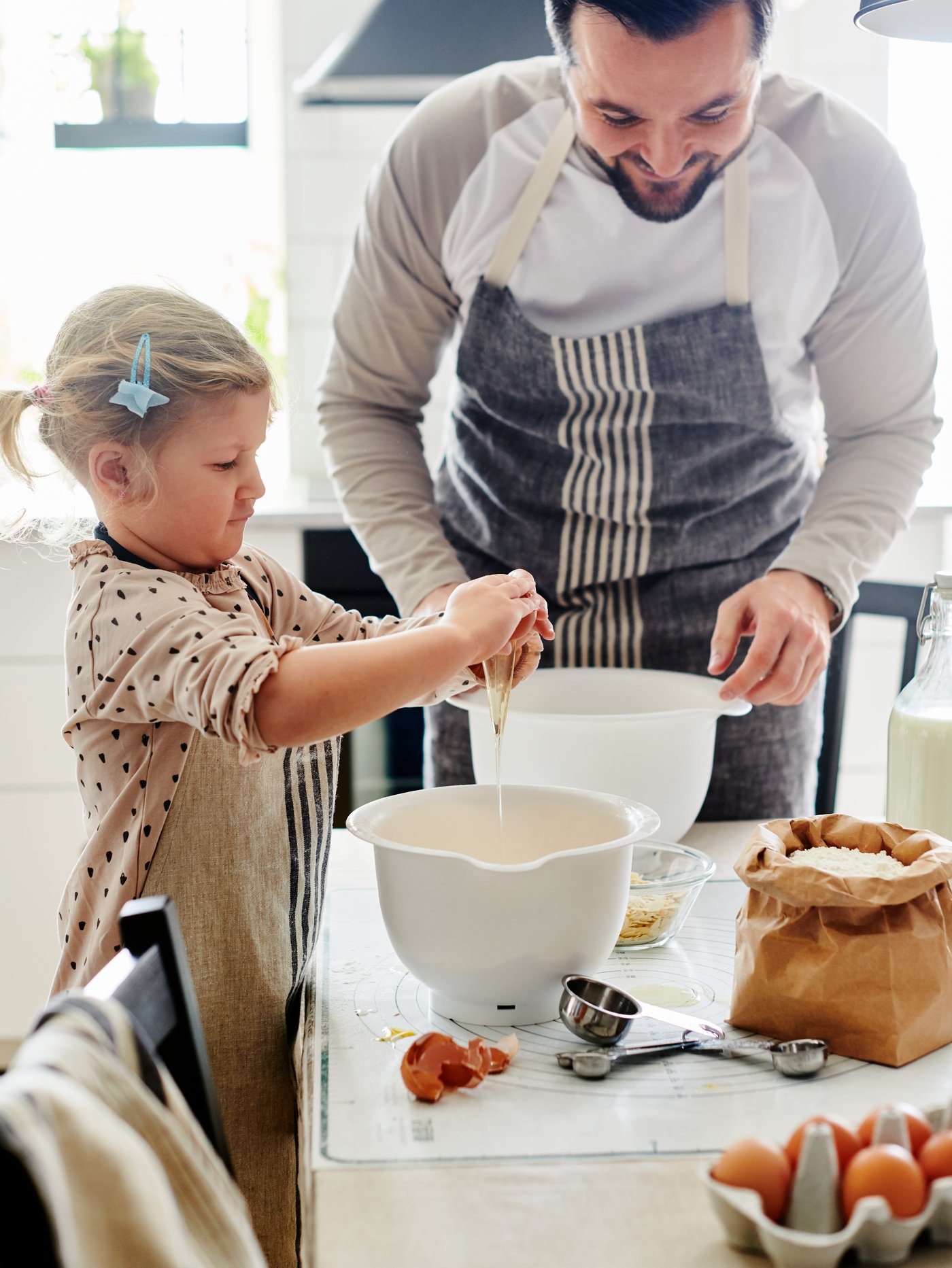 A young girl and a man huddled over a baking project including white VISPAD mixing bowls, eggs, flour and baking accessories.