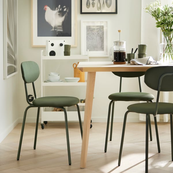 Una mesa de comedor con una cafetera y otros artículos para desayunar. La mesa tiene 3 sillas de comedor ÖSTANÖ verdes.