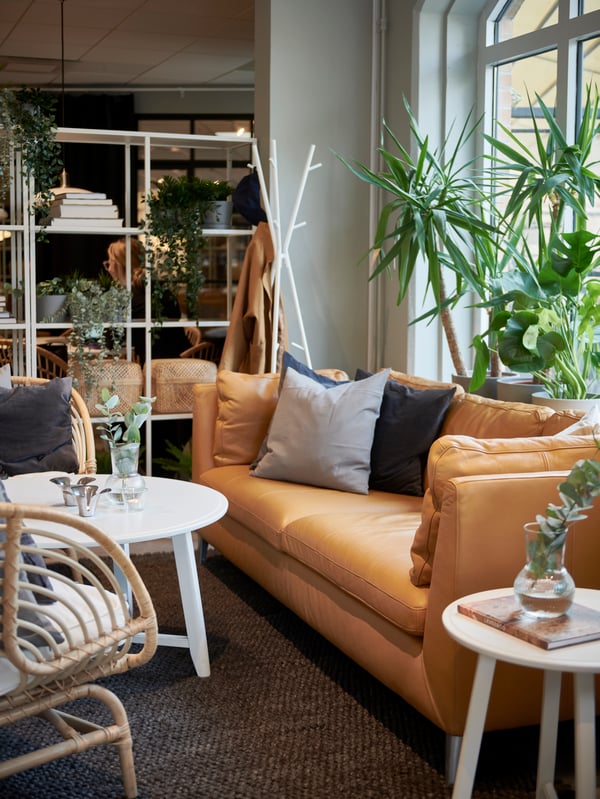 En ljusbrun IKEA STOCKHOLM skinnsoffa sedd från sidan framför ett fönster. Framför soffan står ett vitt, runt soffbord och en BUSKBO fåtölj på en mörkgrå matta. 