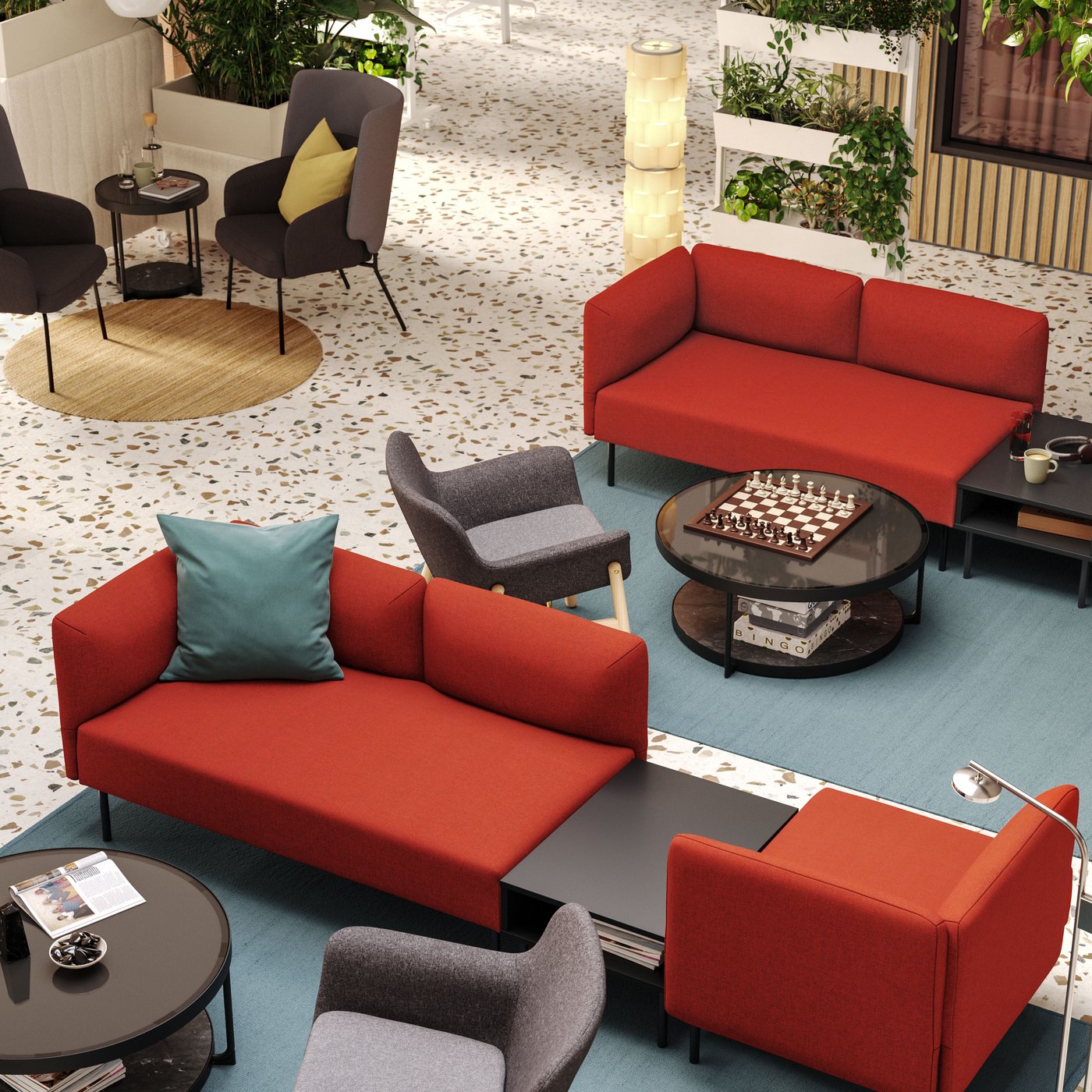 An aerial view of a hotel lobby with two seating areas defined by red LILLEHEM modular sofas and grey armchairs on big rugs.