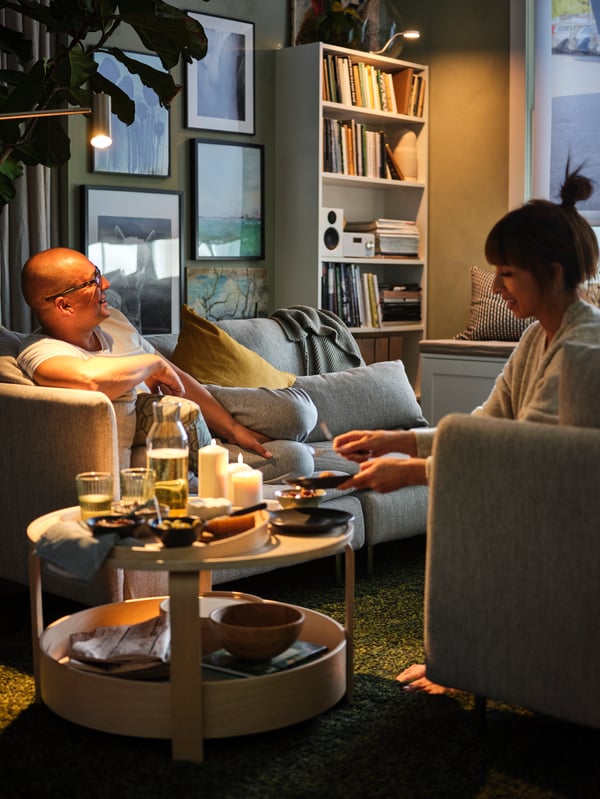 A living area with two adults on parallel SÖDERHAMN 3-seat sofas with a BORGEBY coffee table with snacks, drinks and candles.