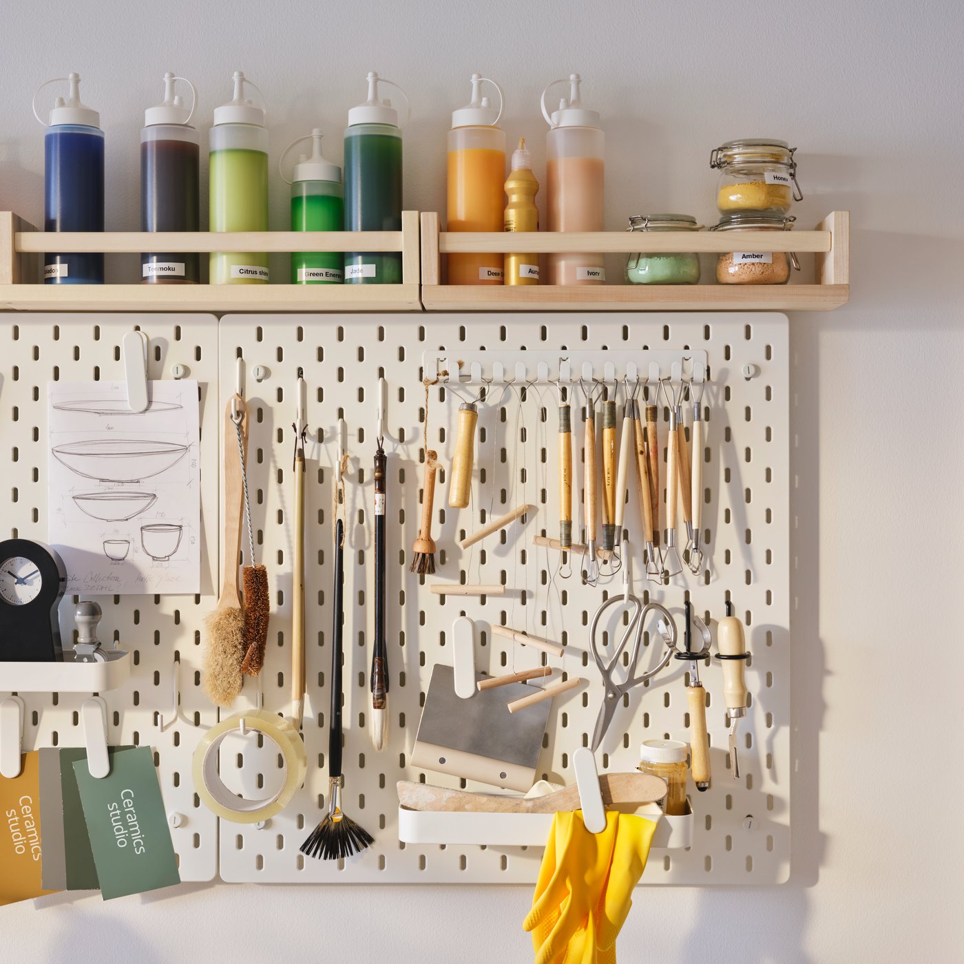 A wall storage solution comprised of a SKÅDIS pegboard for pottery tools and a BEKVÄM spice rack for storing glazes.