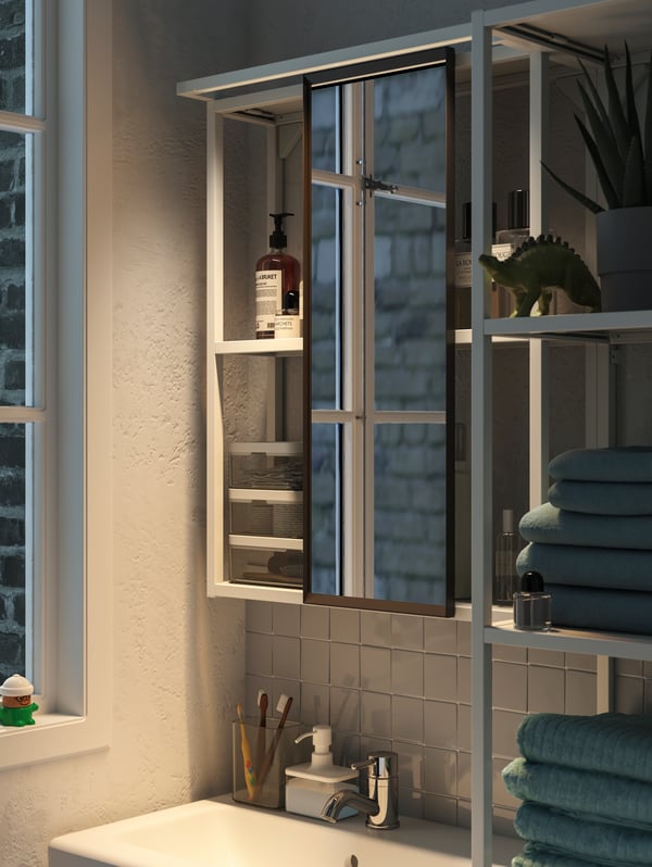 A bathroom cabinet with white frames, a sliding mirror and LED lighting turned on, casting a warm glow in the room.