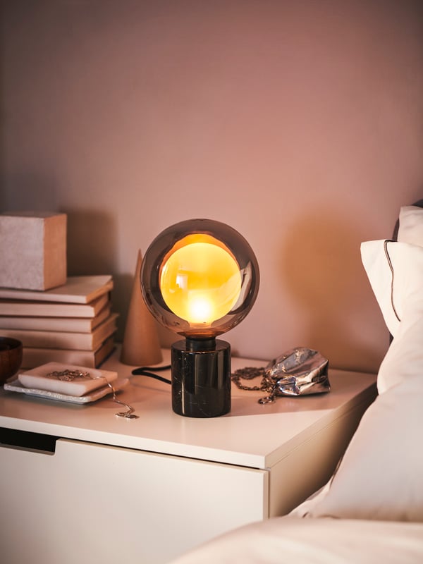 Lampada da terra/lettura SKURUP nera accanto al letto, vicino a una finestra con tende DYTÅG grigio scuro e a una lampada da tavolo TÄRNABY - IKEA.