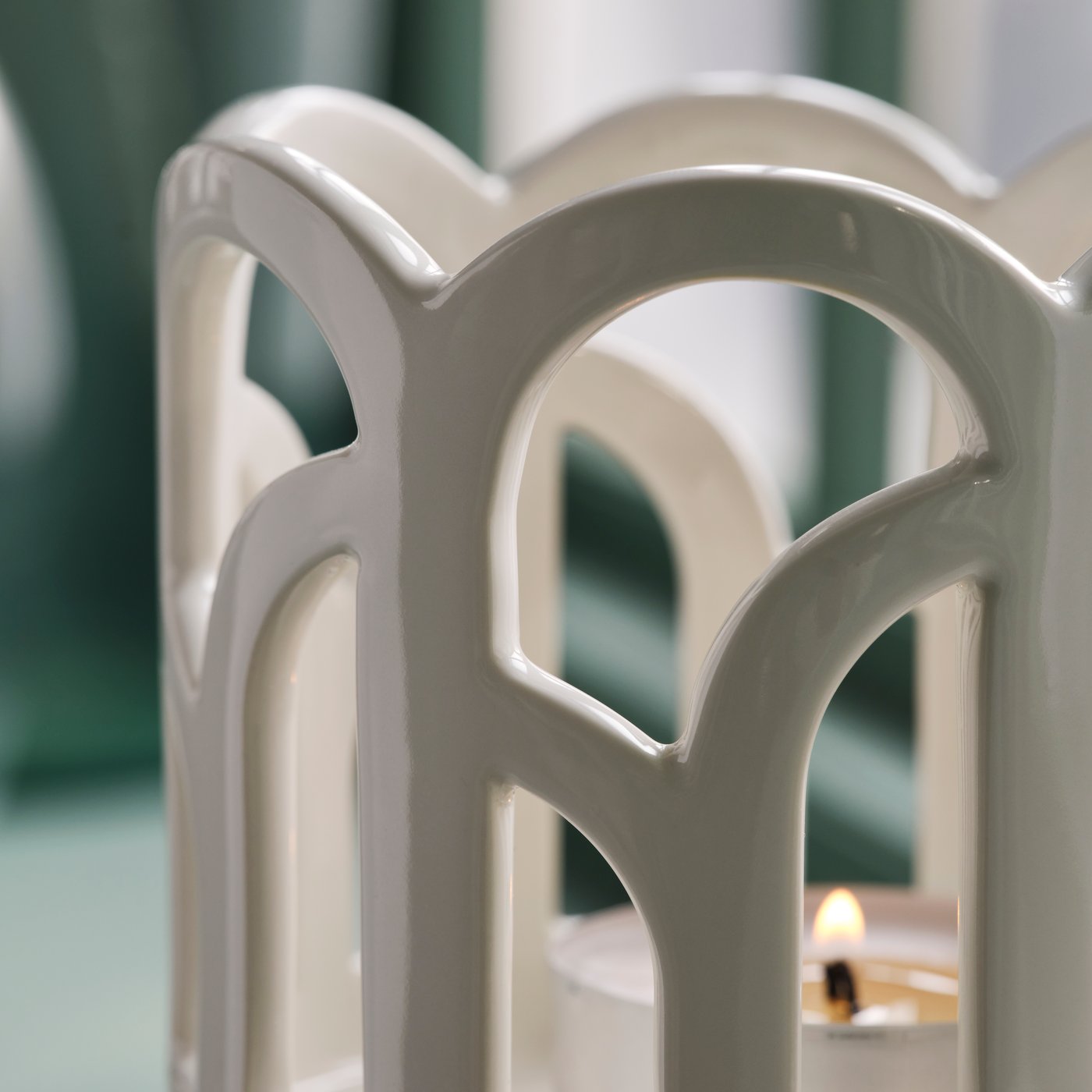 A close-up of a SNÖSISKA candle holder in off-white. The pigmented glaze on the stoneware shines when it catches the light.