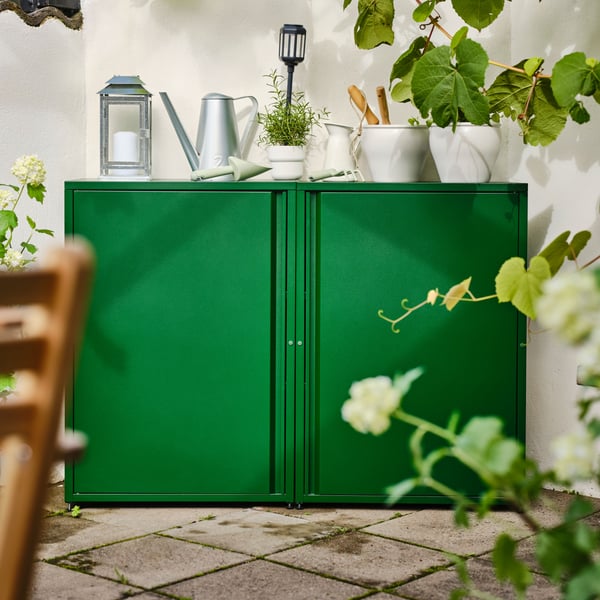 Deux armoires SUNDSÖ vertes installées côte à côte, sur lesquelles sont posés des outils de jardinage et des plantes en pot.