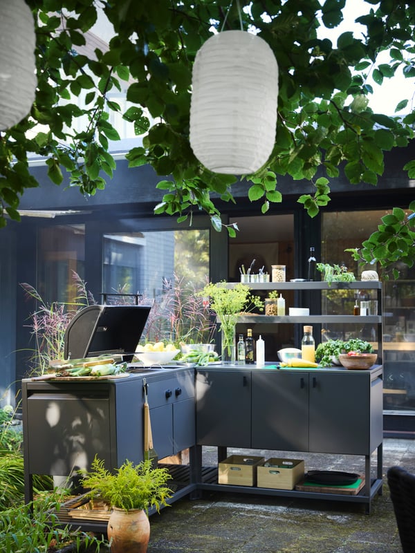 A dark grey BÅTSKÄR outdoor kitchen w charcoal barbecue outside