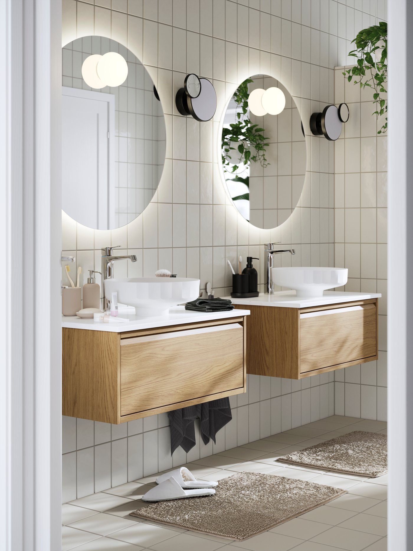 Modern bathroom with dual sinks on an oak-finished ÄNGSJÖN wash-stand with drawers, round mirror, and hanging plants.