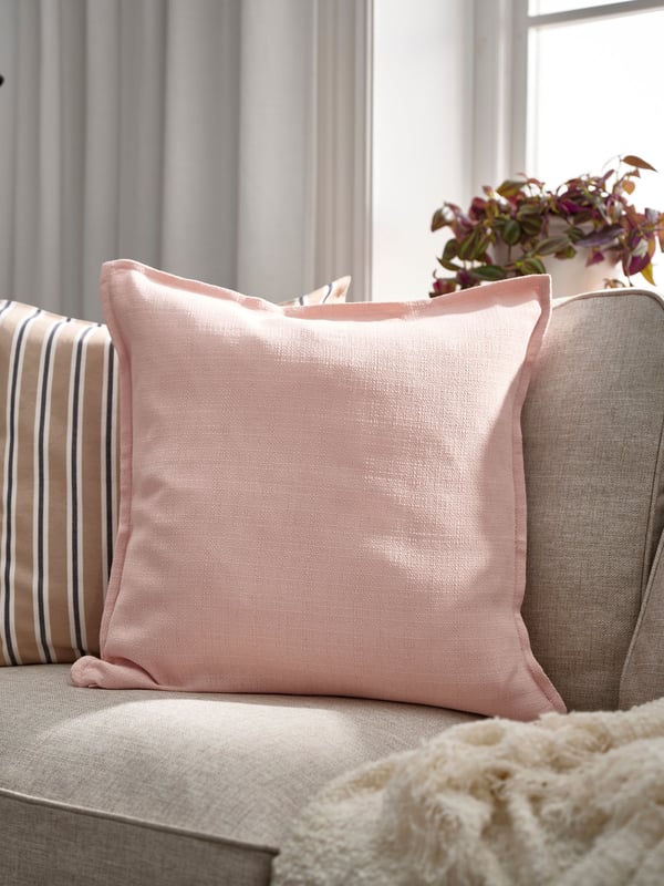 En ljusrosa LAGERPOPPEL kudde i en beige soffa.