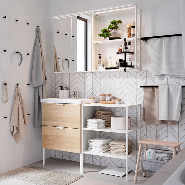 An airy, white-tiled bathroom features an ENHET / ENHET cabinet in oak and white with two drawers and shelves under a mirrored cabinet.
