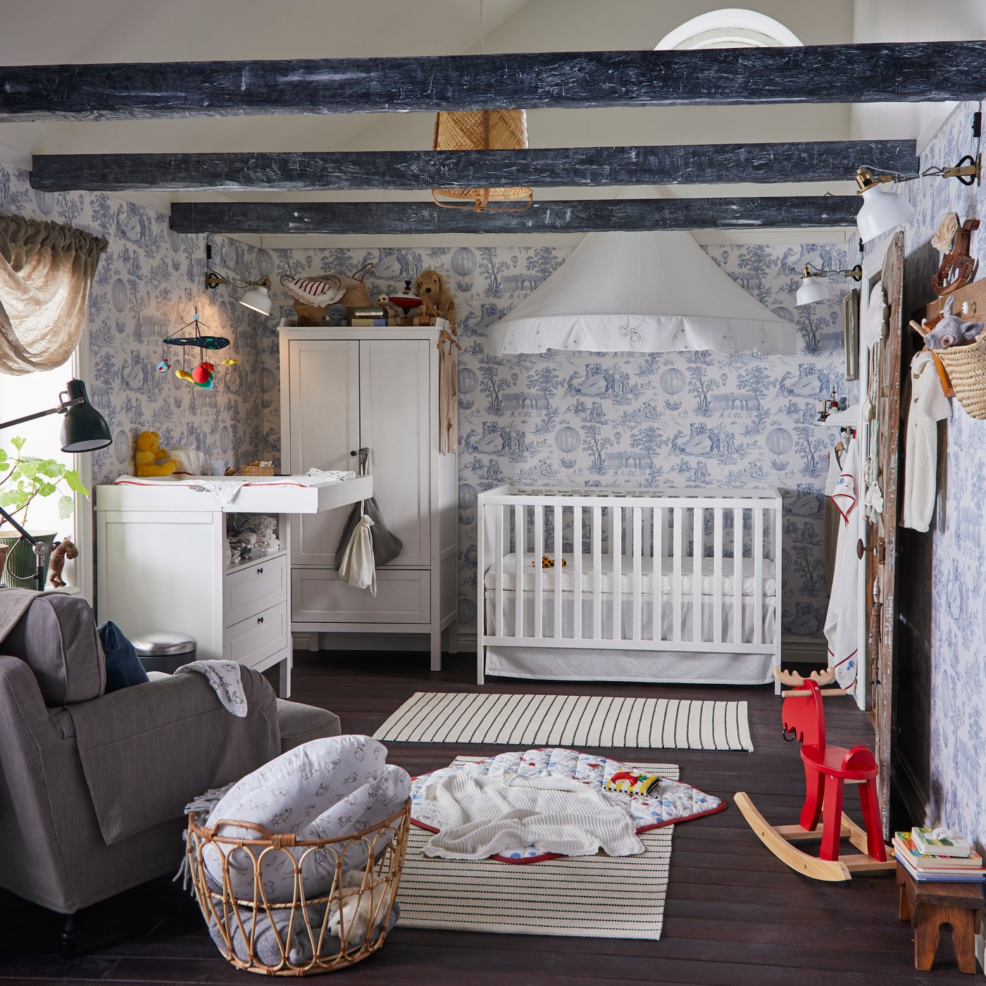 Ein traditionelles Babyzimmer mit weißem Kleiderschrank, Babydecke, Spielbereich, Leseleuchte und Wickeltisch.