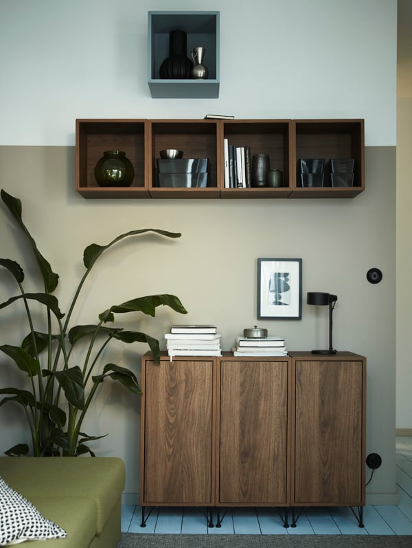 Five EKET wall-mounted shelving units are mounted on a wall above other EKET storage with legs standing on the floor.