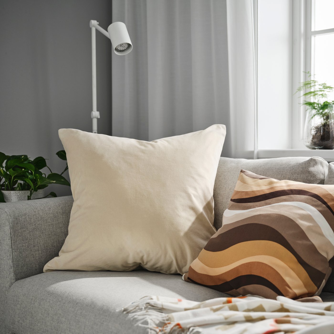 A light beige SANELA cushion cover on a grey sofa in the living room.