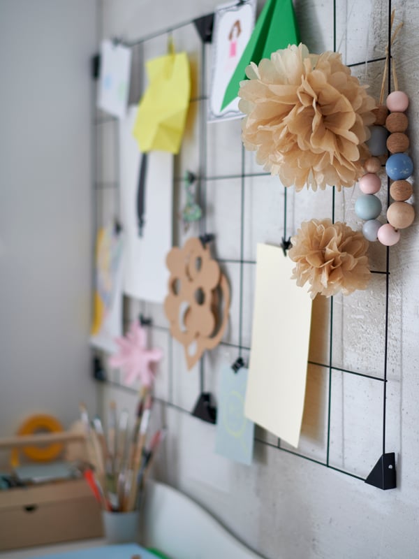 Un tableau-mémo avec pinces SÖSDALA noir sur un mur blanc, avec différents dessins et travaux d'arts plastiques et manuels qui y sont accrochés.