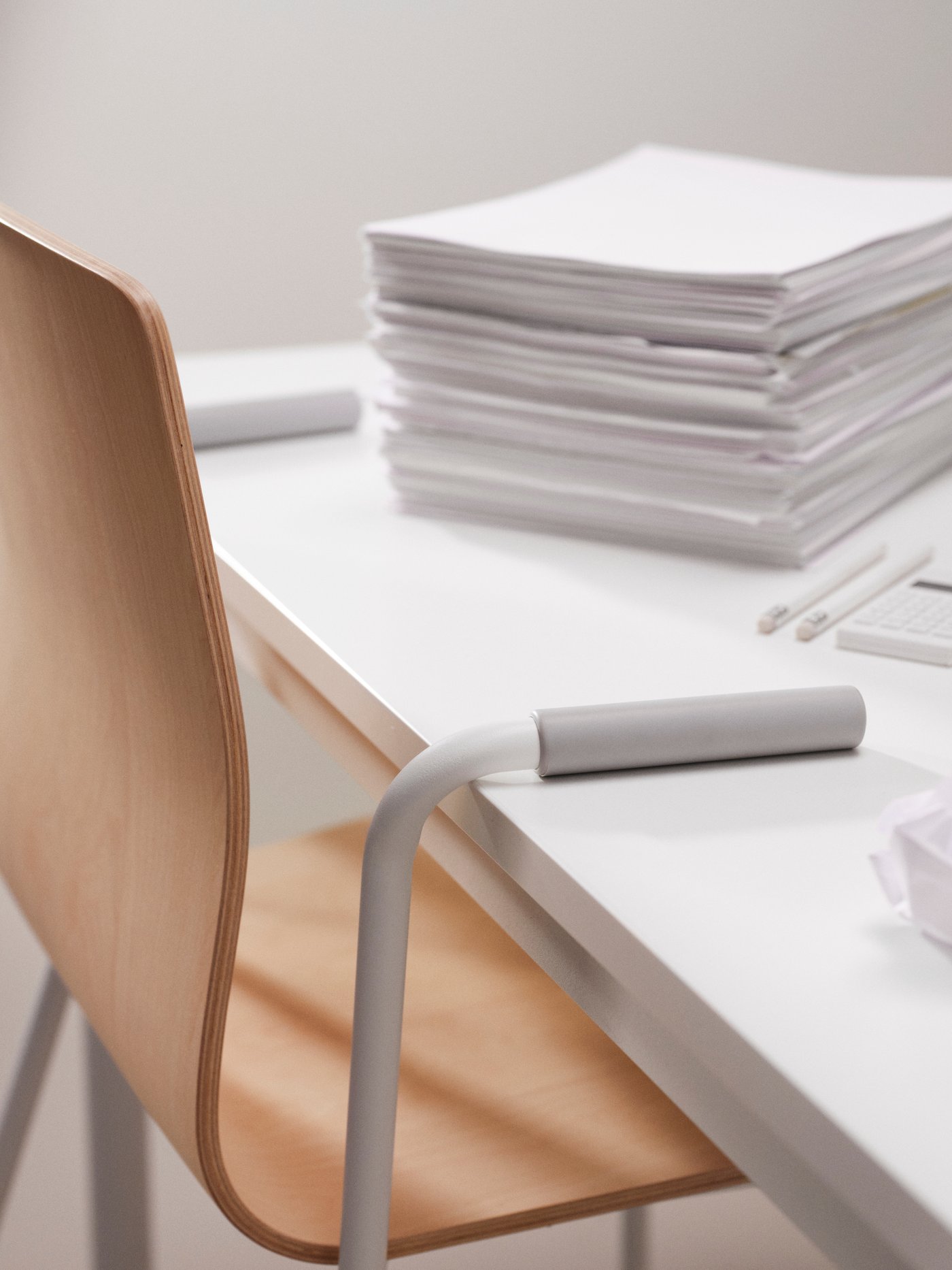 From a table with a stack of papers on it hangs a birch-veneer LÄKTARE chair, its metal armrests resting on the tabletop.