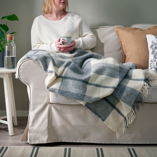 Person relaxing on a sofa under a blanket, showing a simple way to stay warm without turning up the heating.				