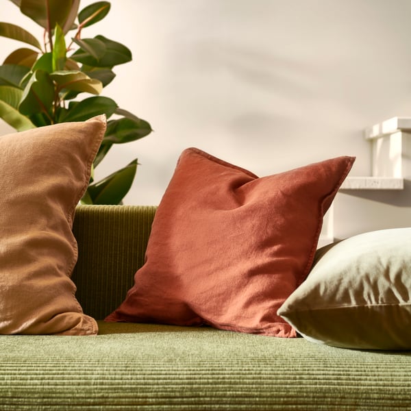 Eine Nahaufnahme des SANELA und DYTÅG Sofakissens auf einer grünen Couch