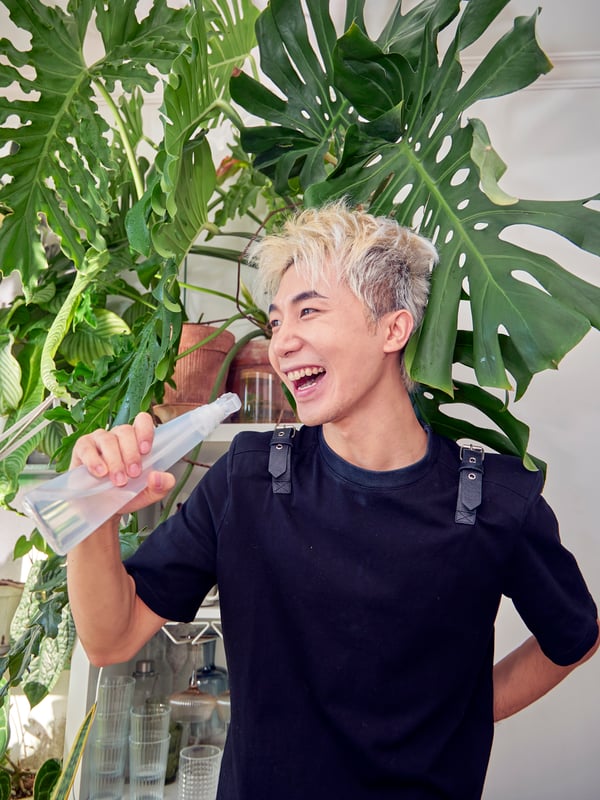 A person is playfully singing into a TOMAT spray bottle, as if it were a microphone.