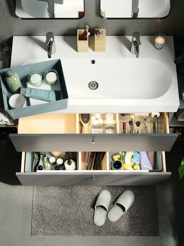 Offene Schubladen mit einer rauchfarbenen GODMORGON Box mit Fächern und grünen Boxen mit Badutensilien.
