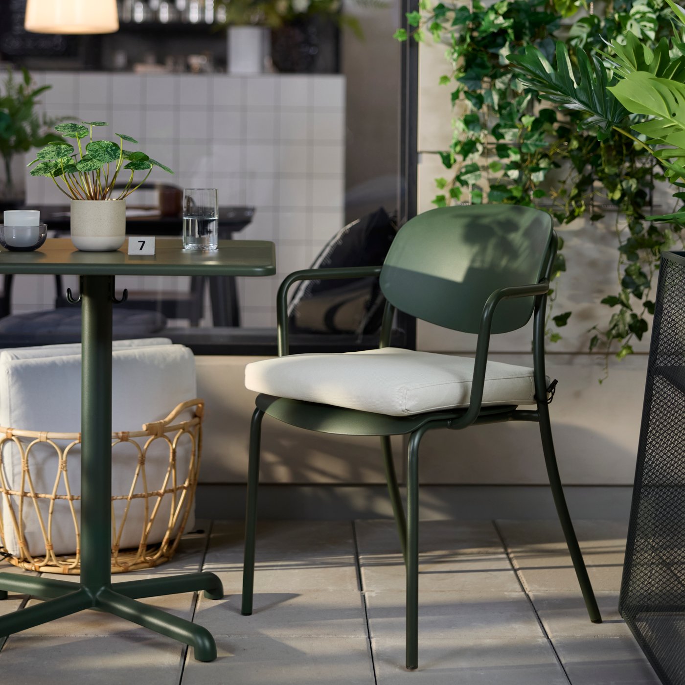 Café outdoor seating with deep green VISINGSÖ table and armchair, surrounded by greenery and outdoor décor.