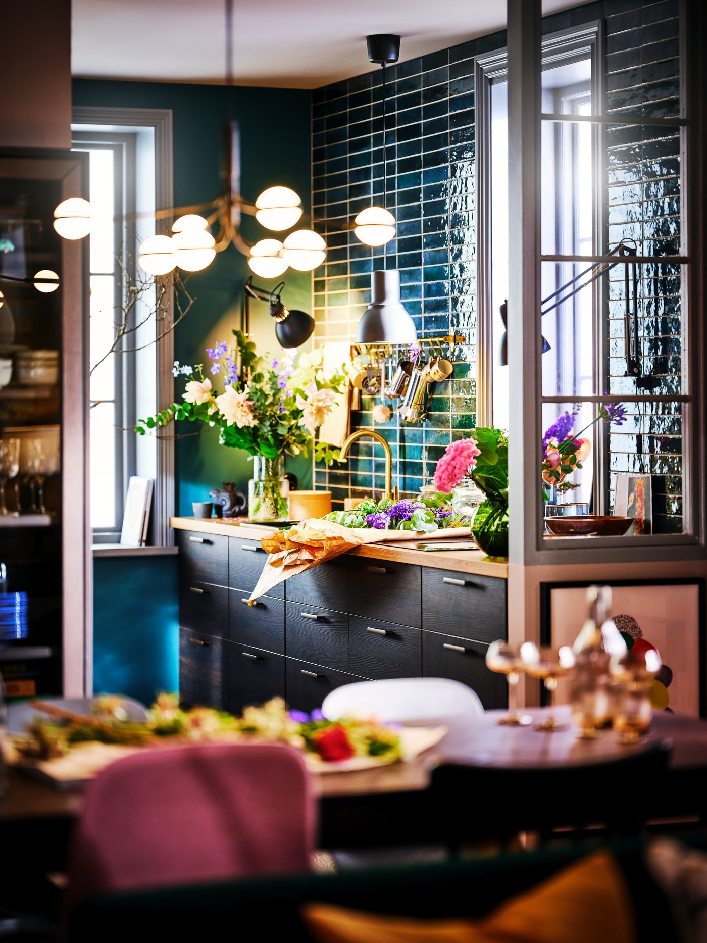 A kitchen with light green STENSUND drawer fronts and two PINNTORP tables surrounded by PINNTORP chairs.