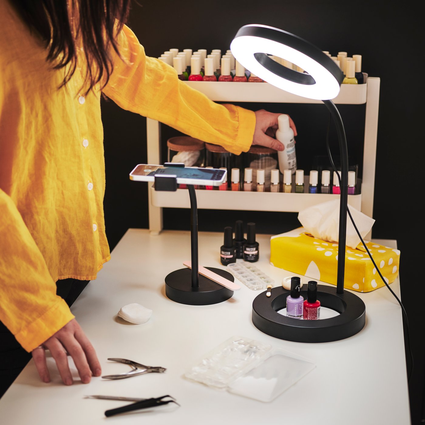 A person in a yellow shirt uses a LÅNESPELARE ring light with phone holder while working on nails at a well-lit table.