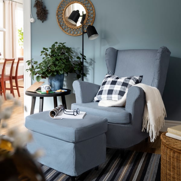 A toy rabbit lies against a cushion on a STRANDMON wing chair with a slipcover with a dark blue/beige stripe pattern.