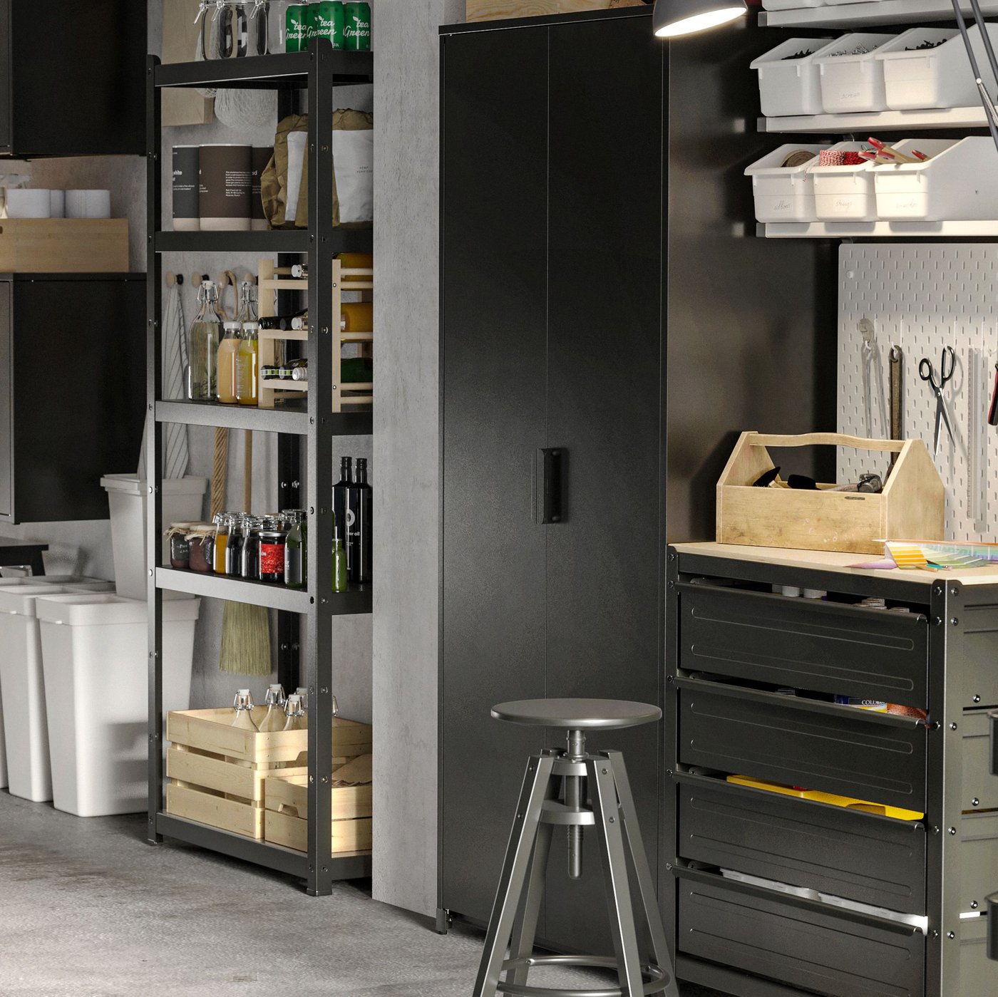 Dans un garage, armoires et rangements ouverts et avec portes en noir. Sur les tablettes, boîtes, flacons et bouteilles. Au sol, bacs de recyclage.