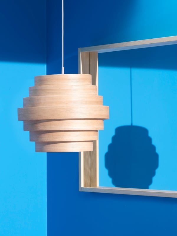 A DYKARKLOCKA pendant lampshade with seven veneer rings hangs in a room with bright blue walls and a square mirror.
