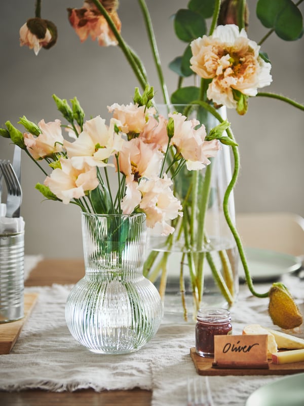 Pink lowers in clear glass vases PÅDRAG on a table. There is a small sign with a name Oliver on it.