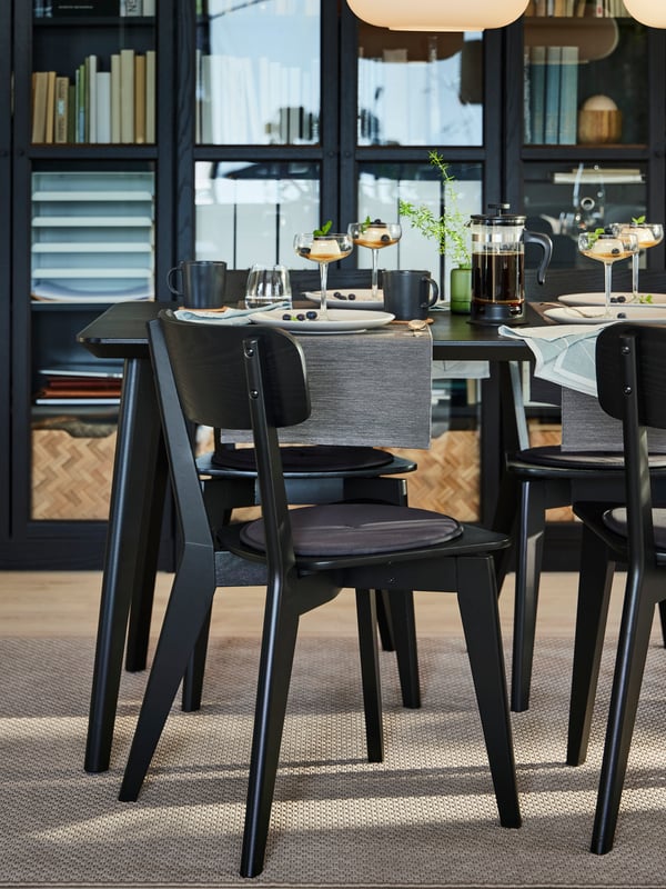 Two black LISABO dining chairs in front of a table that’s laid with plates, bowls, champagne coupes and table runners.