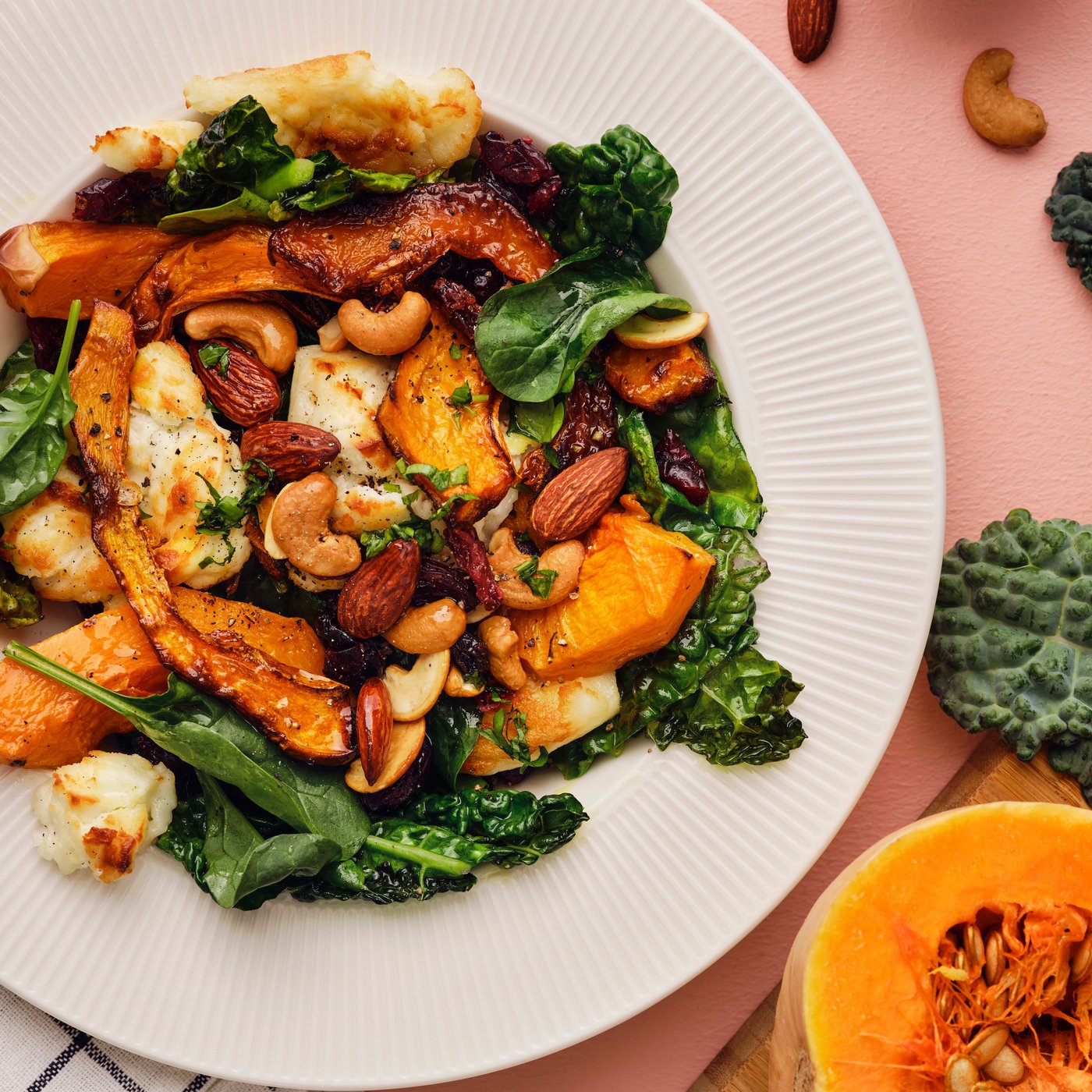 En græskarsalat med butternut squash, palmekål, gedeost og en MUNSBIT blanding af ristede nødder/bær på en hvid tallerken.