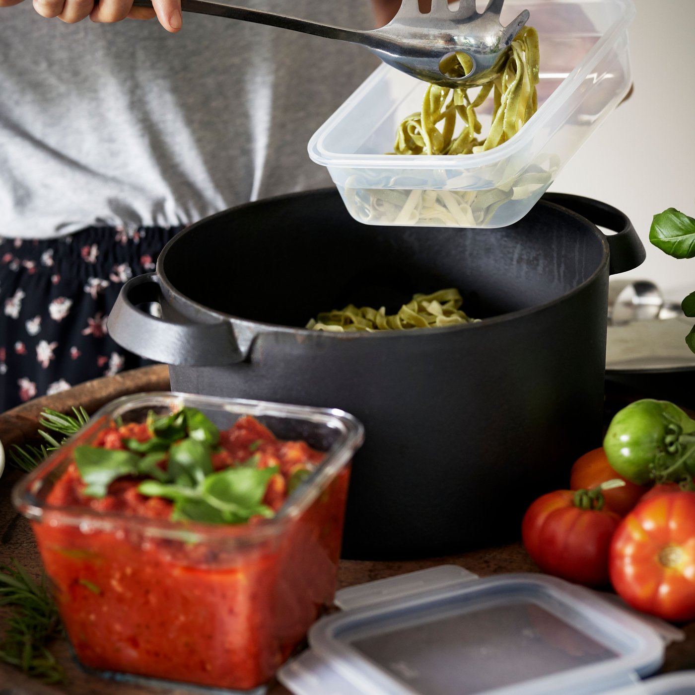 A kitchen setting shows a person using IKEA 365+ food containers to store freshly cooked pasta and tomato sauce.