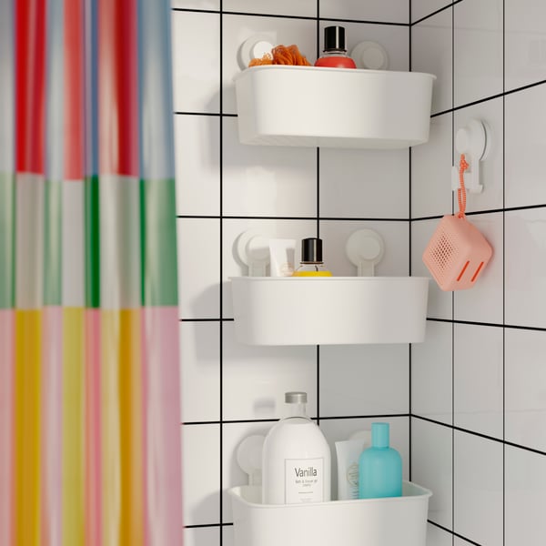Trois paniers à ventouse TISKEN l’un au-dessus de l’autre près d’un rideau de douche multicolore et d’une enceinte WiFi rose.