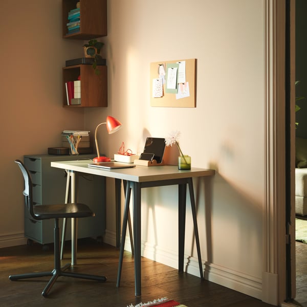 A dimly sunlit corner of a light room, with a minimalistic workspace consisting of a slimline table and a swivel chair.