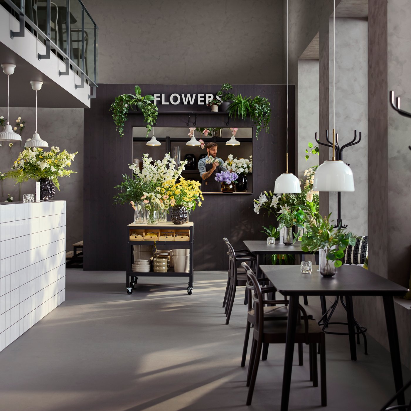 Café environment with natural light featuring tables, chairs and a black/pine BROR trolley displaying flowers and vases.
