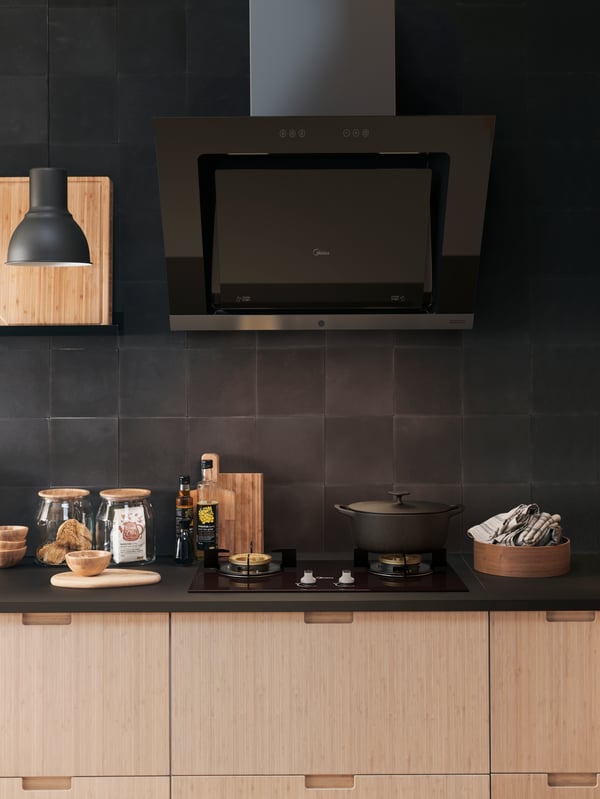 A kitchen cooking area with UPPSVING extractor hood in black and an EKBACKEN counter top.