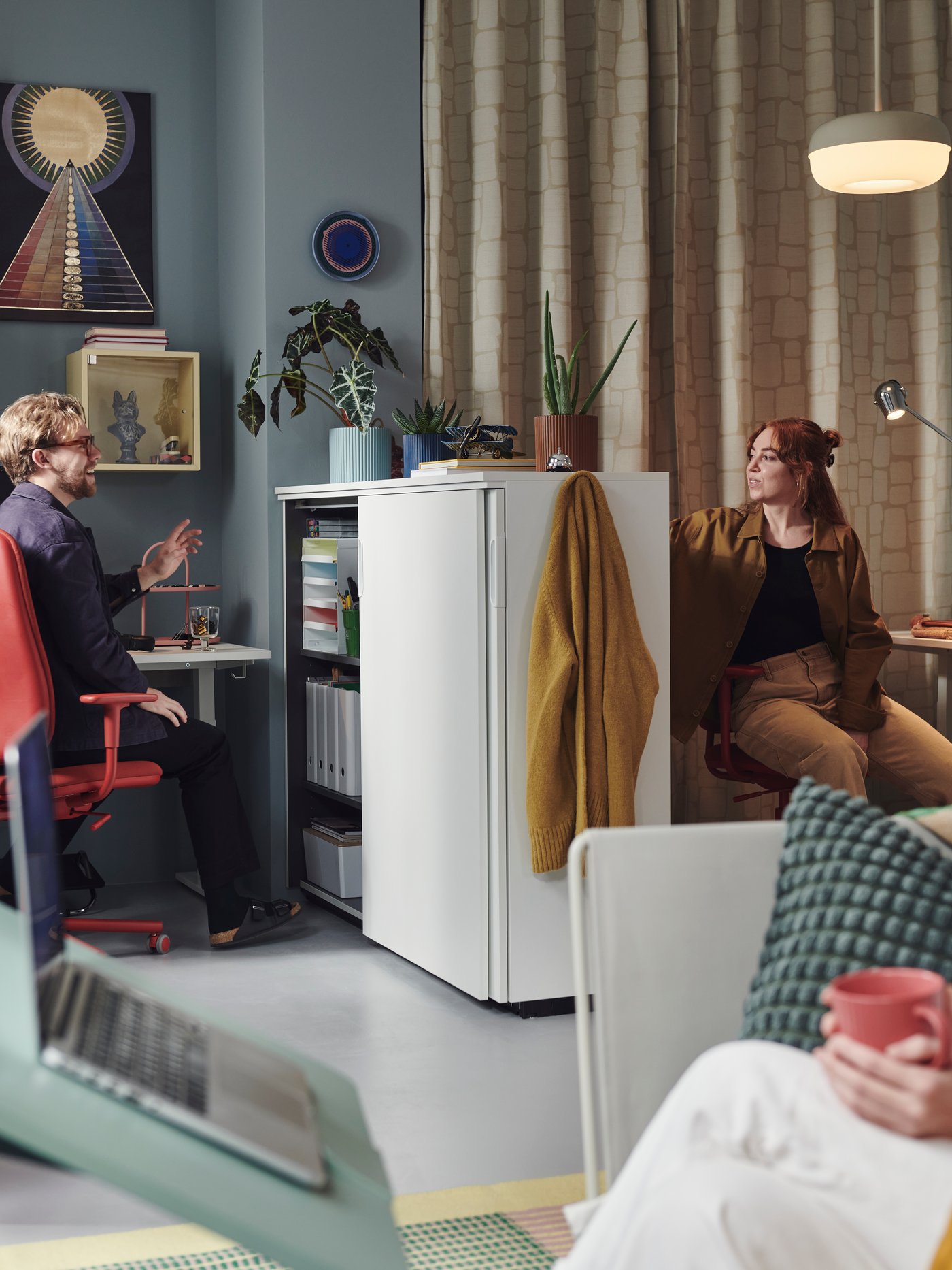 Two people are having a conversation in a modern and vibrant office space. There is a GALANT cabinet in between them.