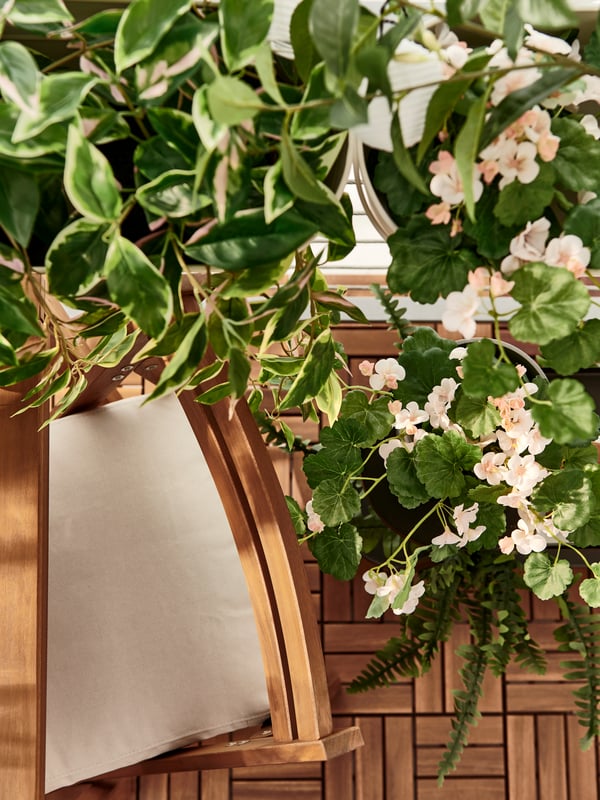 A beige FRÖSÖN/DUVHOLMEN chair cushion on a NÄMMARÖ foldable chair next to a leafy cluster of FEJKA artificial plants.