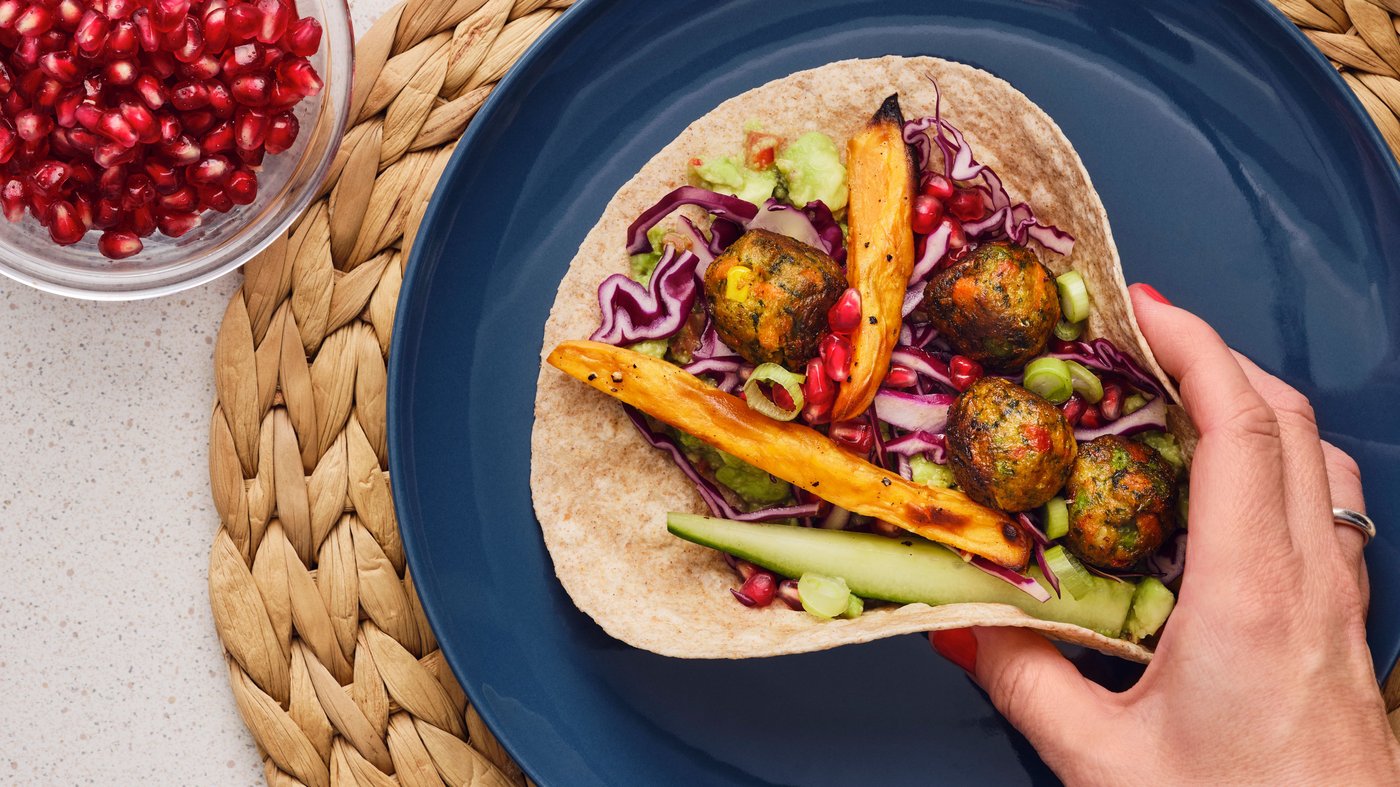 Una persona agarra una tortilla con albóndigas de vegetales y verduras que se encuentra en un plato azul.