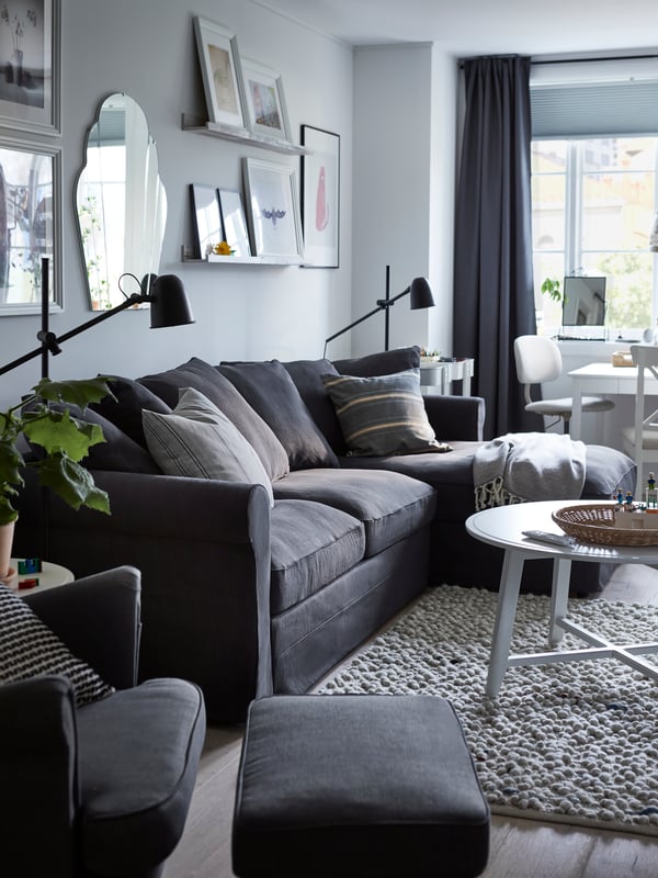 A light living room with a dark-grey GRÖNLID three-seat sofa-bed with chaise longue and a KRAGSTA coffee table beside it.