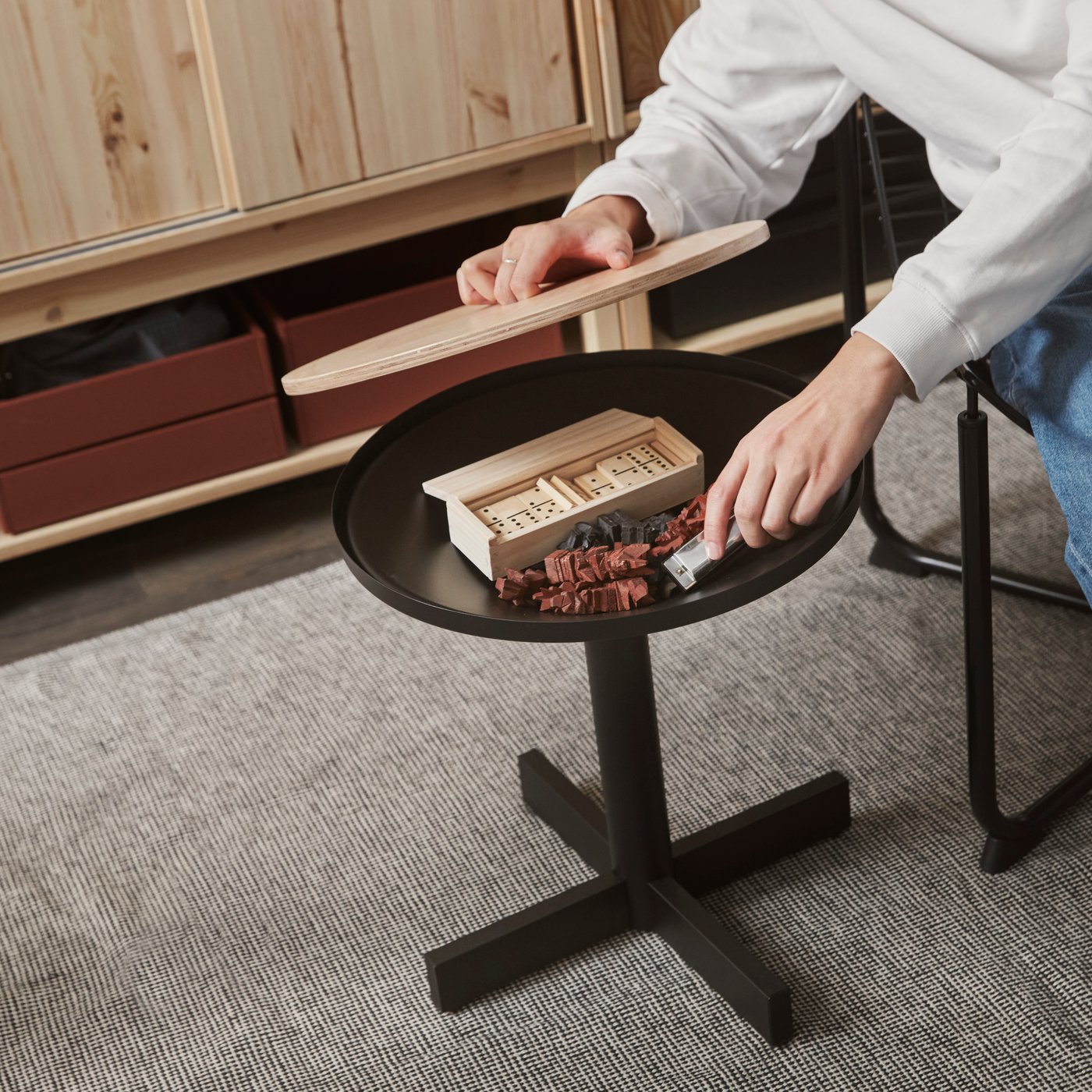 A person is lifting the pine plywood lid from a GRIMSARBO side table in black showing a wooden game underneath in the storage.