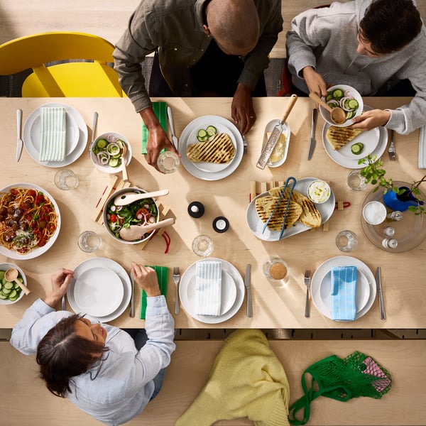 Vue en plongée sur une table BERGSHYTTAN en plaqué bouleau où des personnes partagent un repas dans des assiettes GODMIDDAG blanches.
