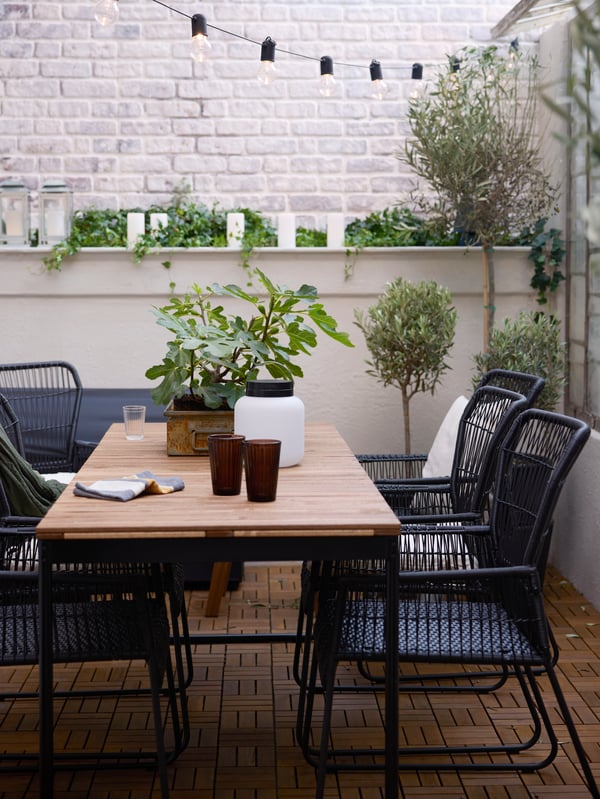 En terrasse med et VÄSMAN udtræksbord omgivet af TALLSKÄR stole med armlæn og en bærbar LÄNSPORT LED-lampe på.