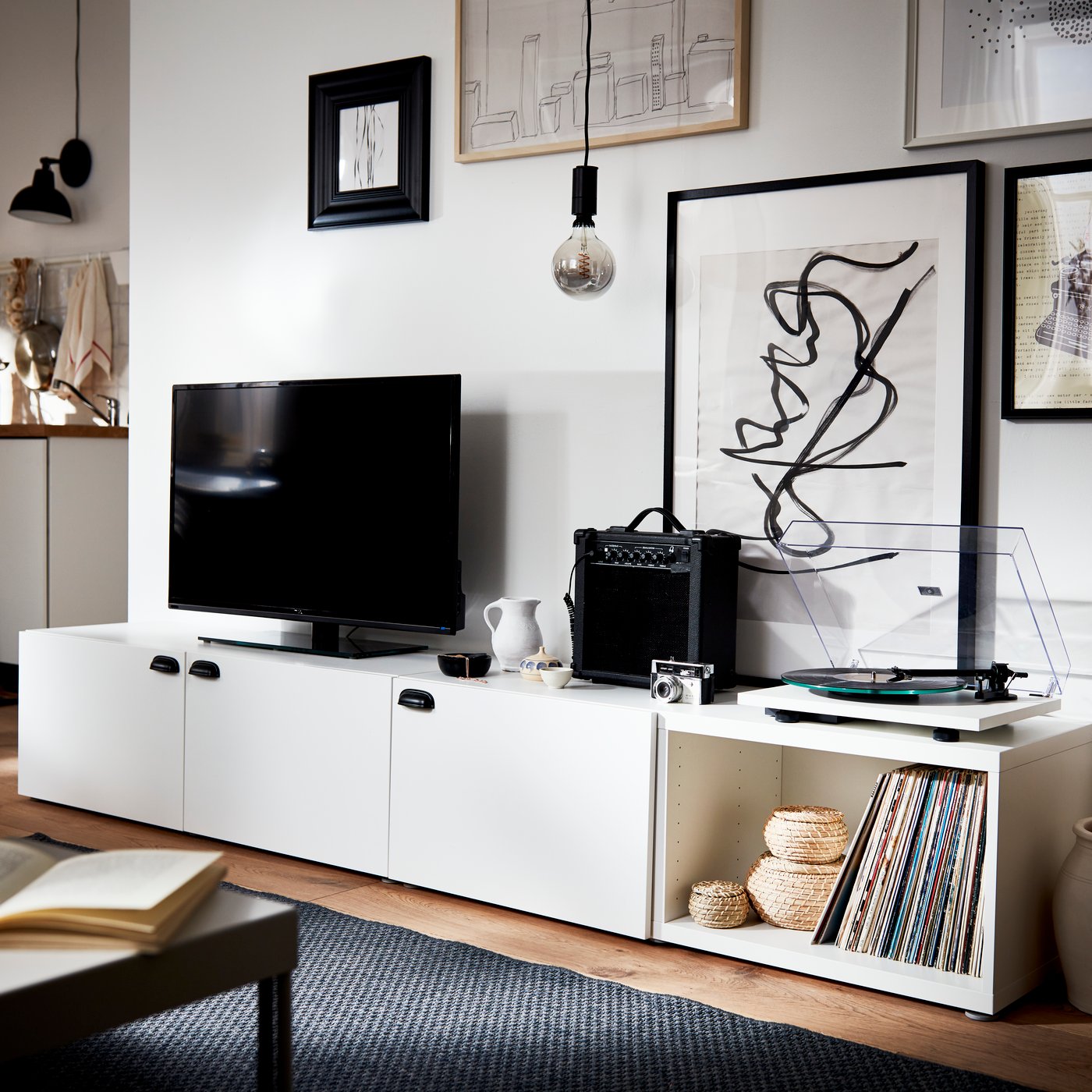 Mueble de TV BESTÅ blanco, con 3 puertas, una sección abierta, con un televisor, un amplificador y un tocadiscos en la superficie.