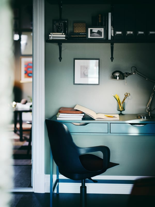 An ODGER swivel chair in front of a grey-turquoise ALEX desk with a FORSÅ work lamp below a BERGSHULT/KROKSHULT wall shelf.