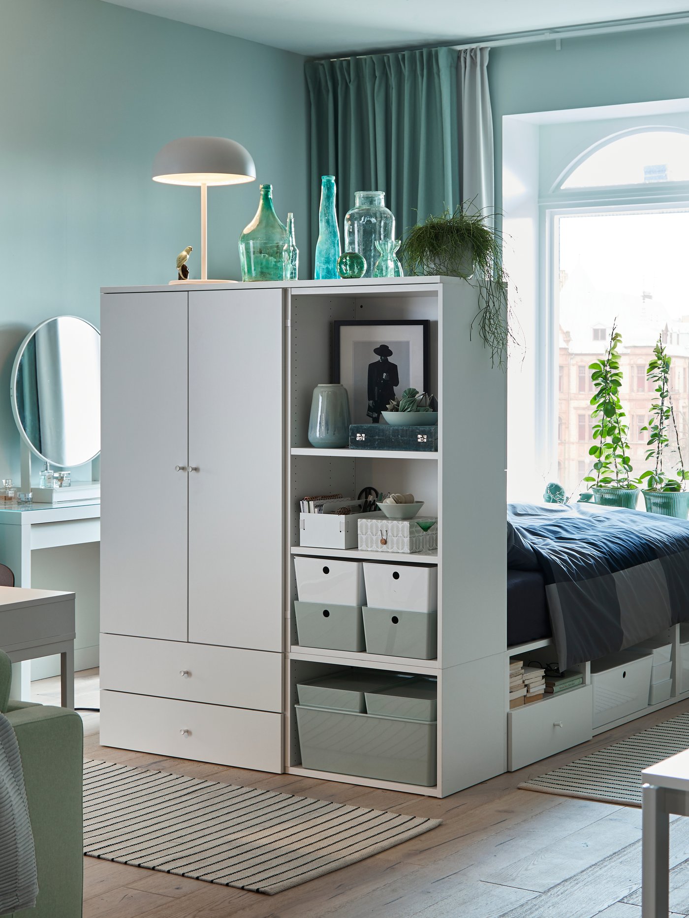 Einzimmerappartment in hellen Grüntönen, einem Sofa in Hellgrün und einem weißen Bettgestell mit Aufbewahrung