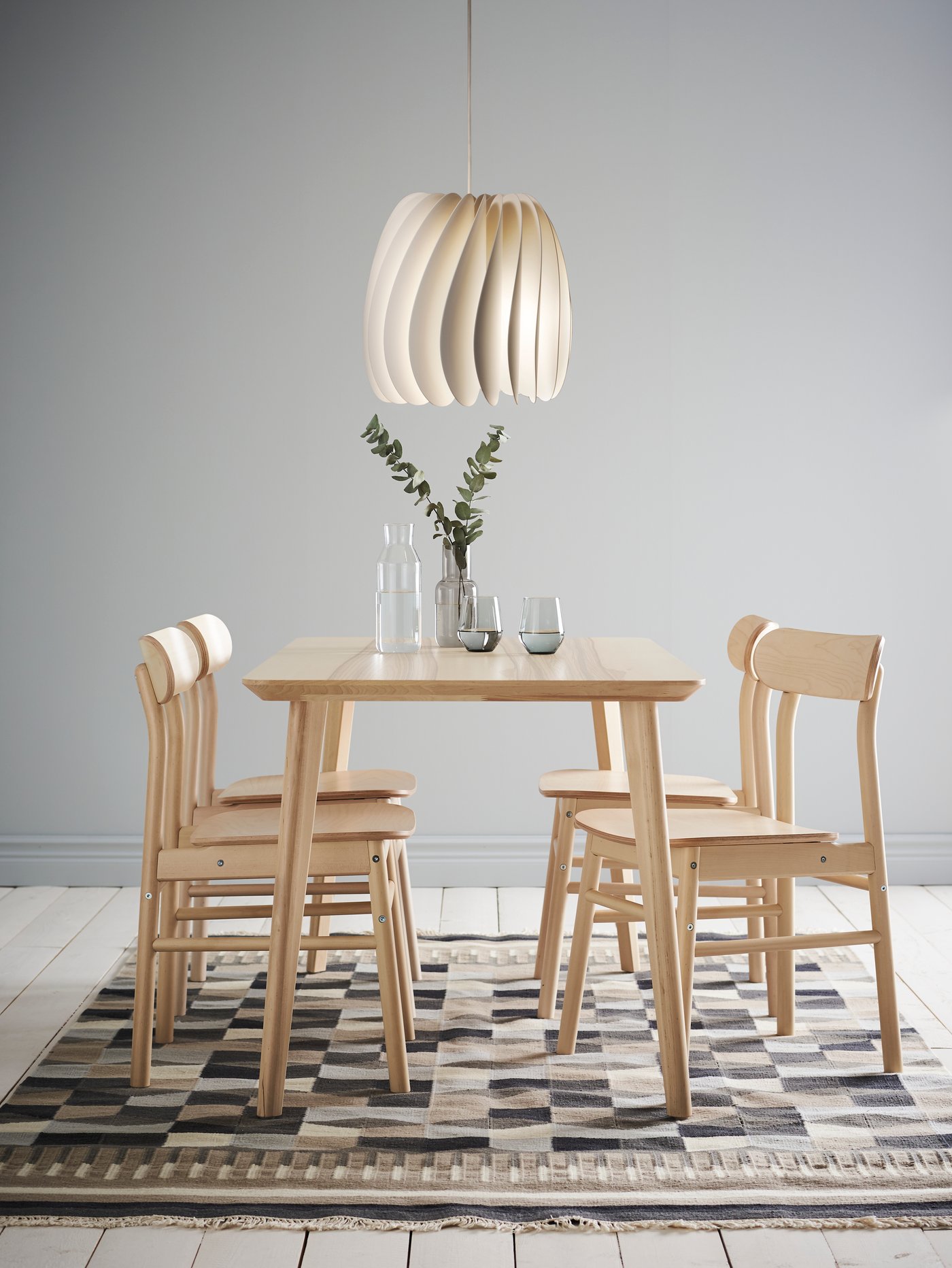 Un ensemble de salle à manger « LISABO », composé d’une table et de quatre chaises en placage de frêne et de bouleau, est disposé sur un tapis. La table est garnie de verres et d’un vase.