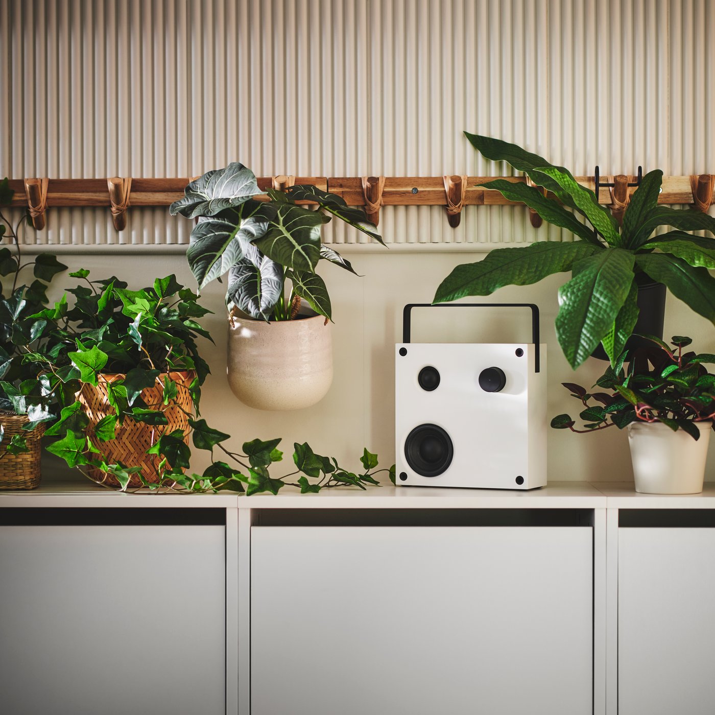 A white VAPPEBY Bluetooth speaker on top of a BISSA shoe cabinet surrounded by various FEJKA artificial potted plants.