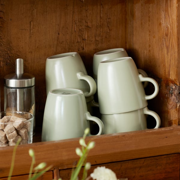 An IKEA walnut larder featuring FÄRGKLAR matt light green cups, DOLD sugar shaker and an IKEA365+ glass cup filled with brown sugar cubes.